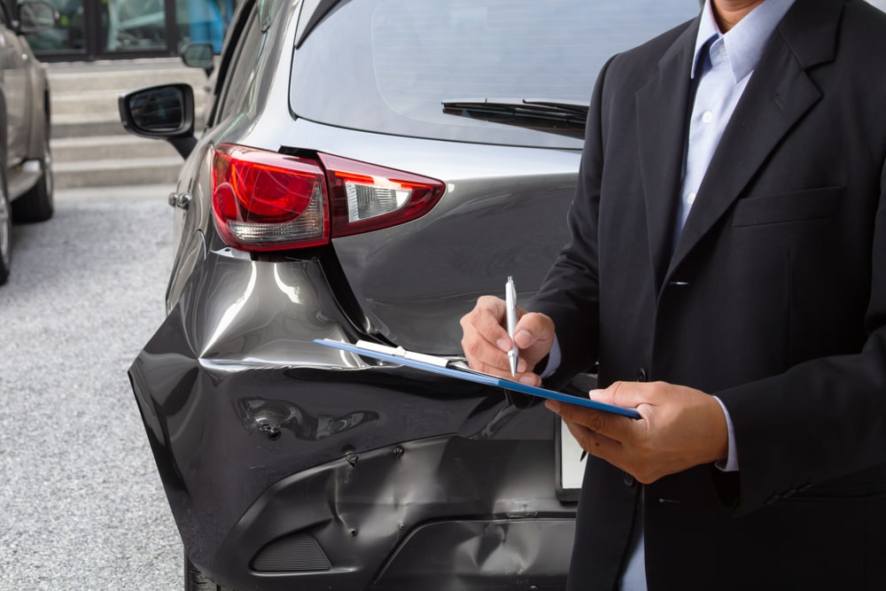 Side view of insurance officer writing on clipboard while insurance agent examining black car after accident. Car accident attorney in New Orleans