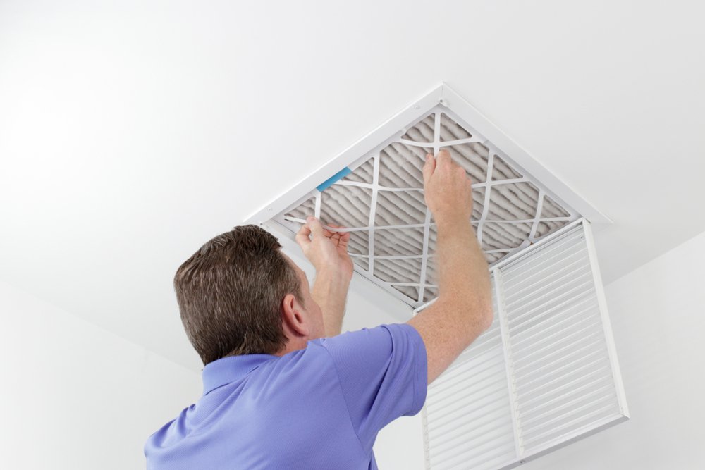 HVAC professional in New Orleans replacing a dirty air filter from a home's ceiling vent, ensuring clean and efficient air flow.