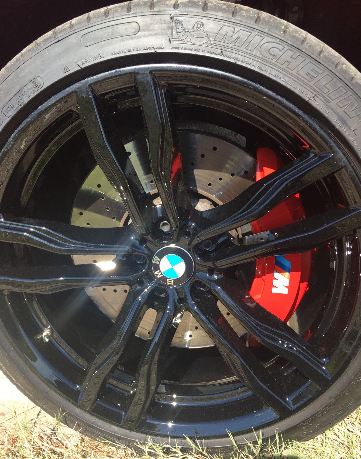 Close-up of a Michelin tire on a BMW with black rims and red brake calipers, highlighting Kenner automotive services quality at Armadillo Automotive