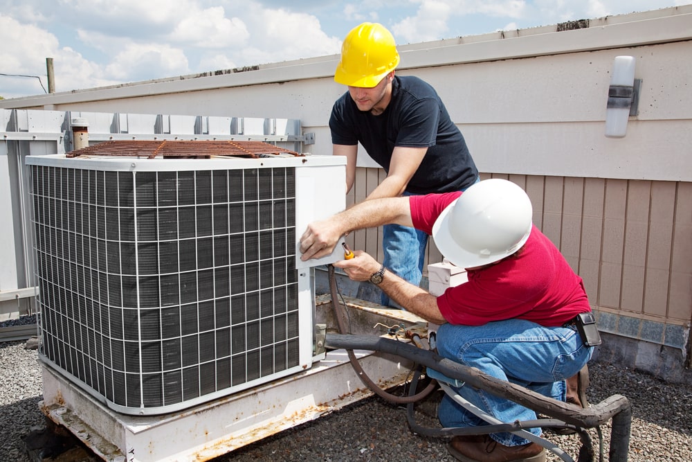 Two workers on the roof of a building installing an air conditioning unit. New Orleans hvac service provider