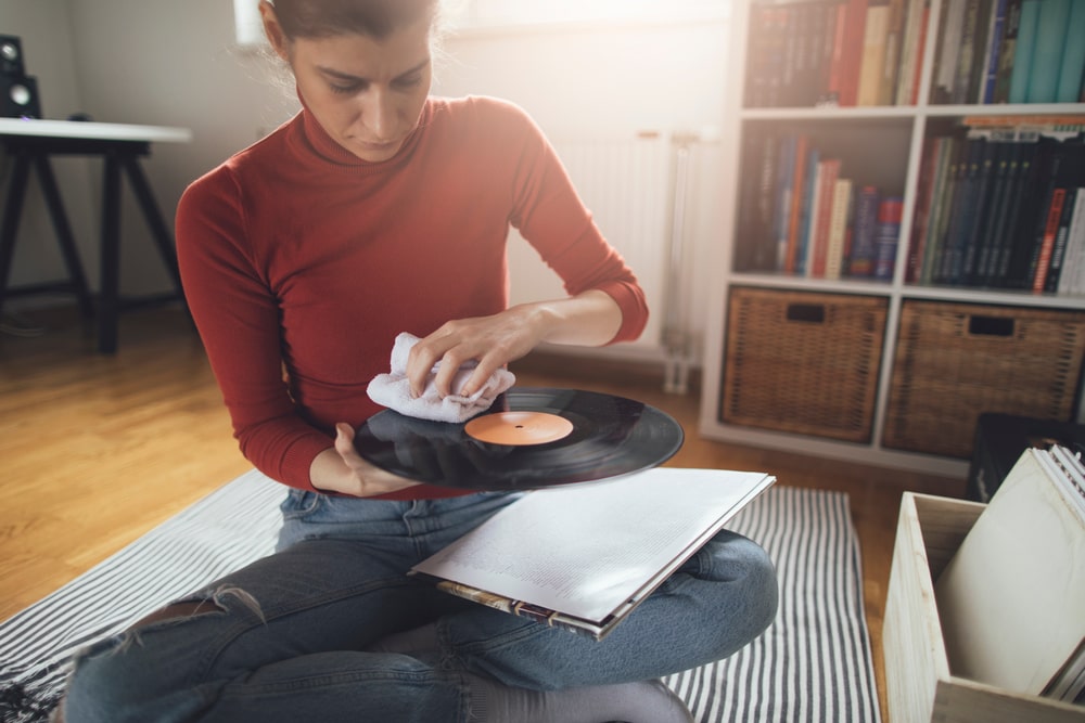 Young girl cleaning dust form her vinyl record collection, showing the need of an electronic repair store